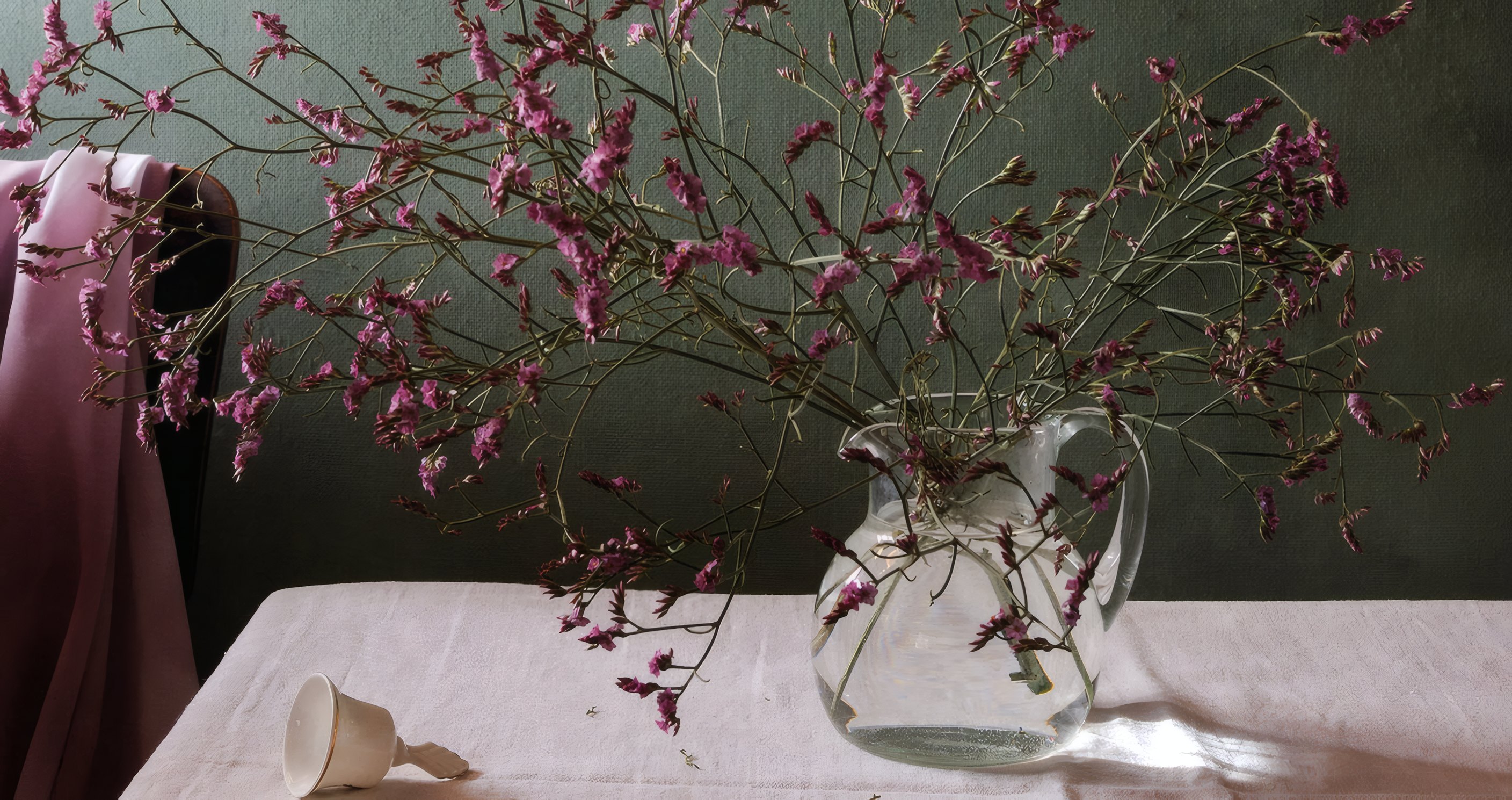 Pink tamarisk branches in a glass pitcher on a linen cloth