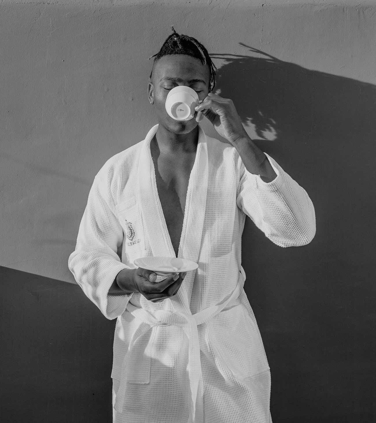A man in a white waffle robe drinking coffee