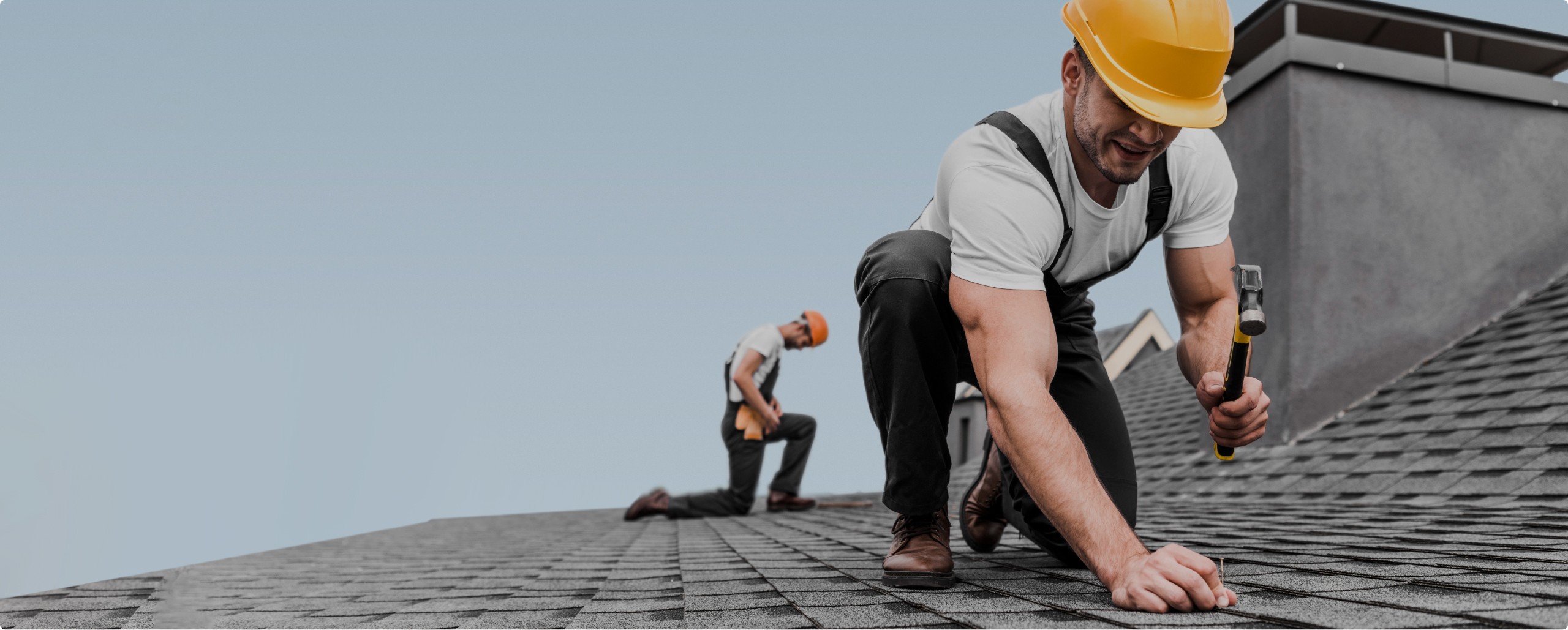 Two roofers in hard hats fixing tiles on a roof