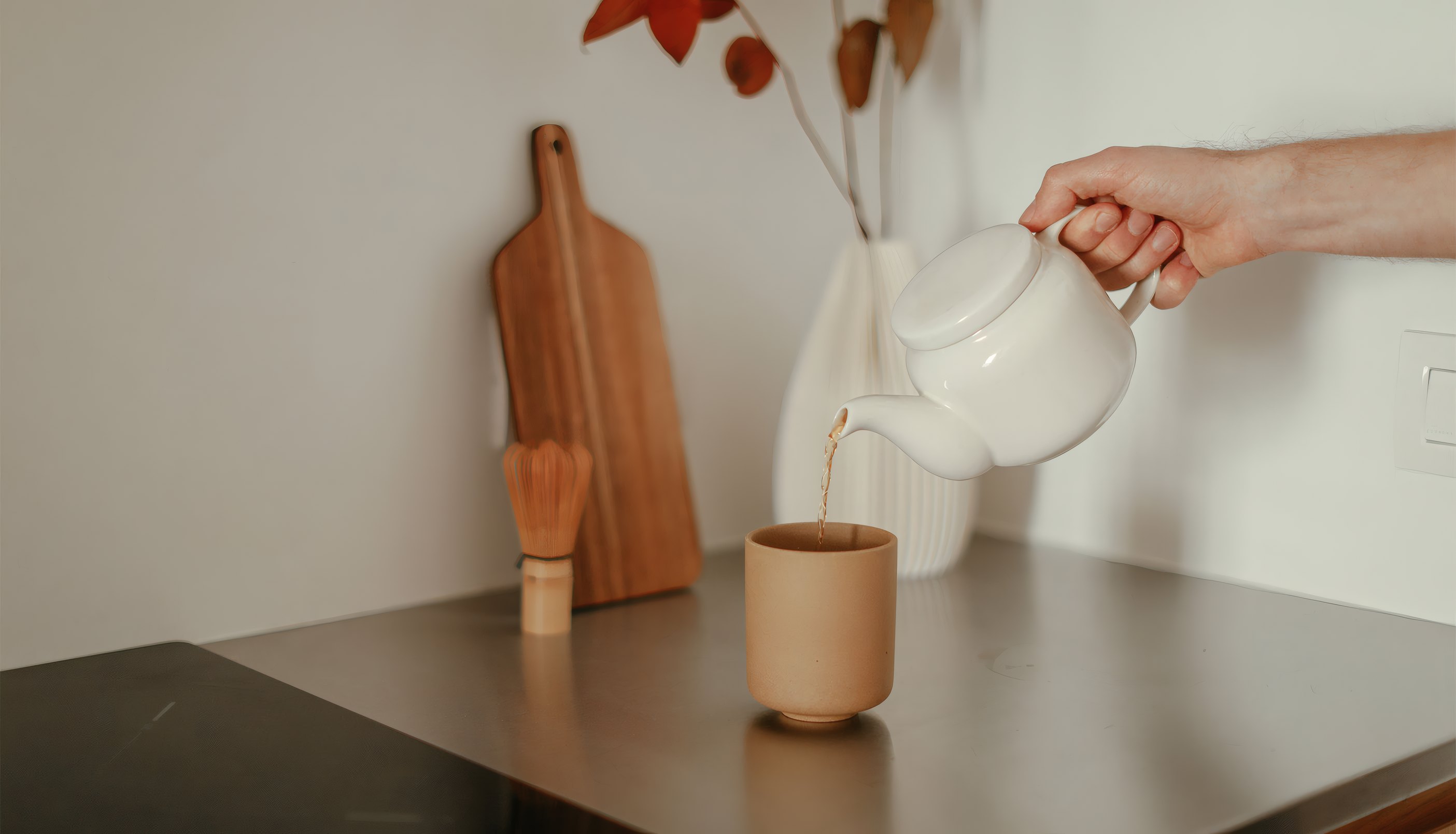Tea poured from a white pot into a clay cup