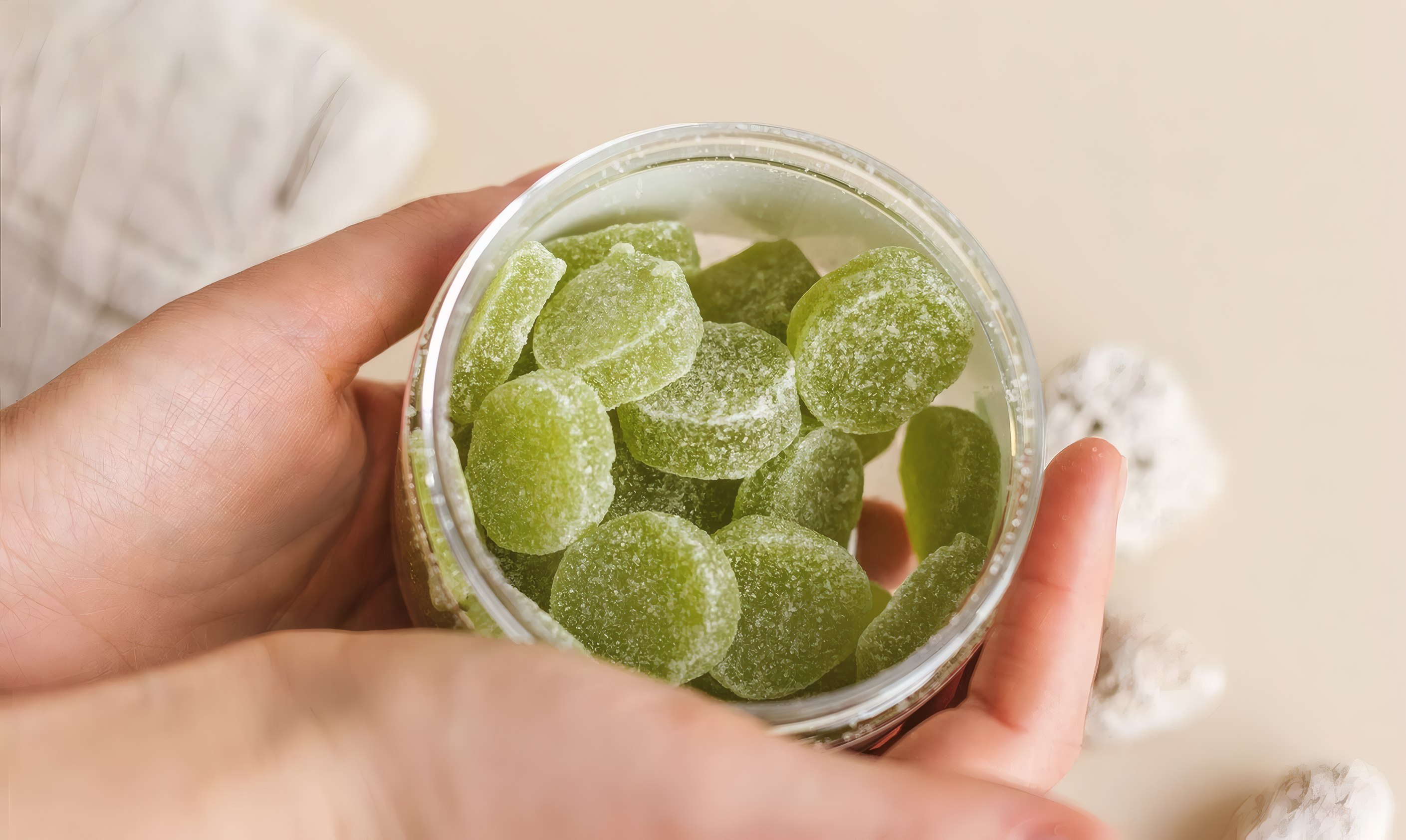 Hands holding a jar of green gummies