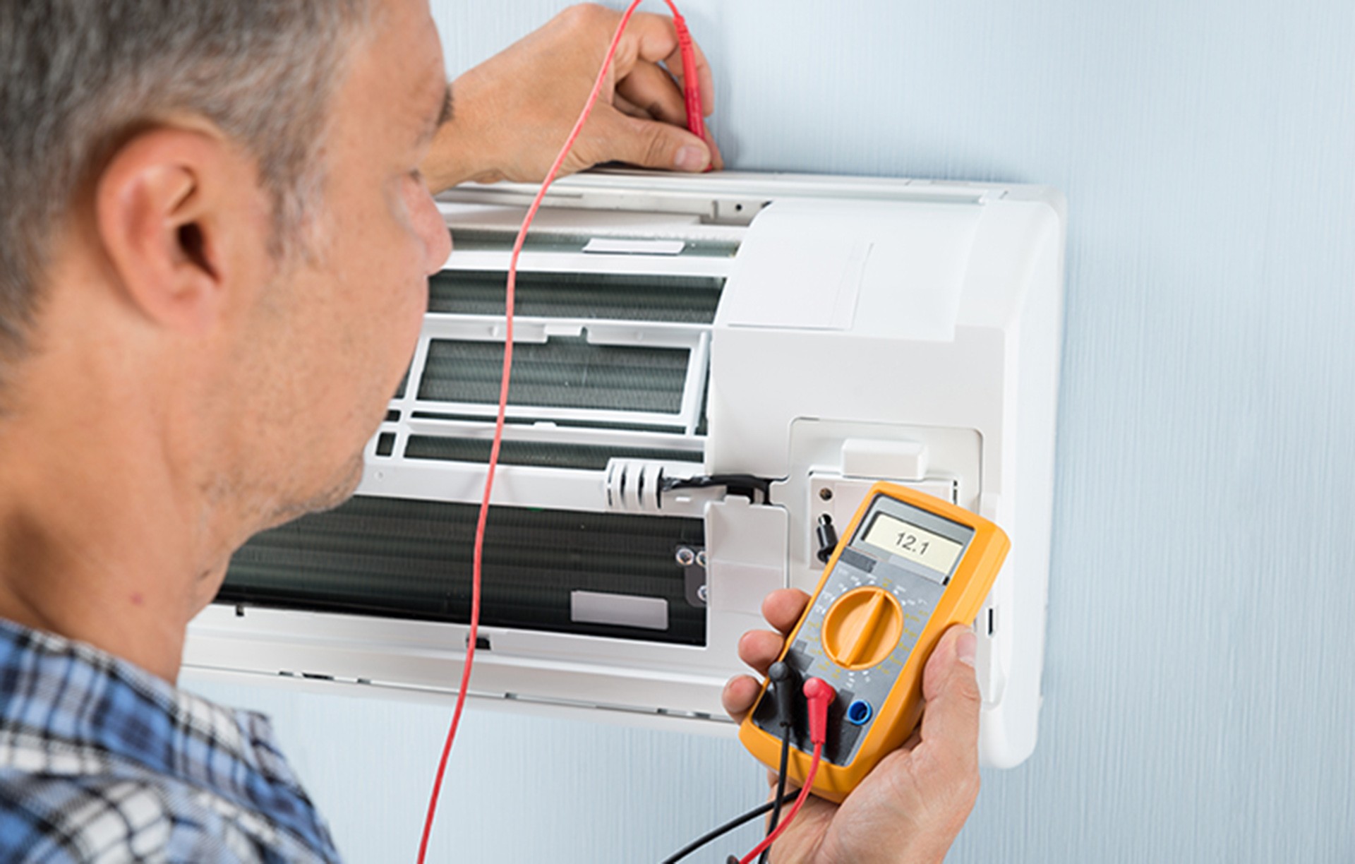 A fitter testing a split air conditioner with a multimeter