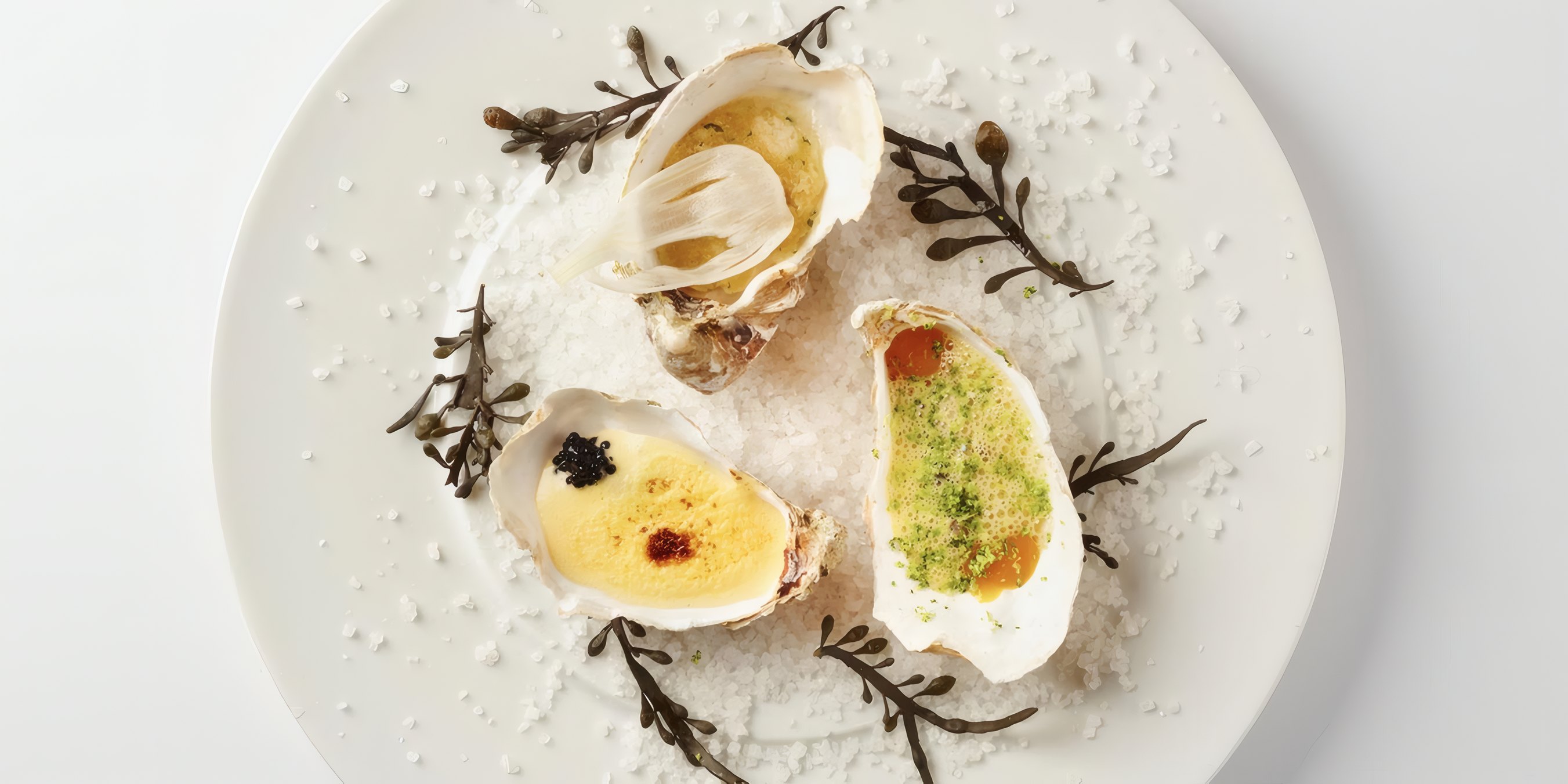 Three oysters with caviar and herbs on a white plate
