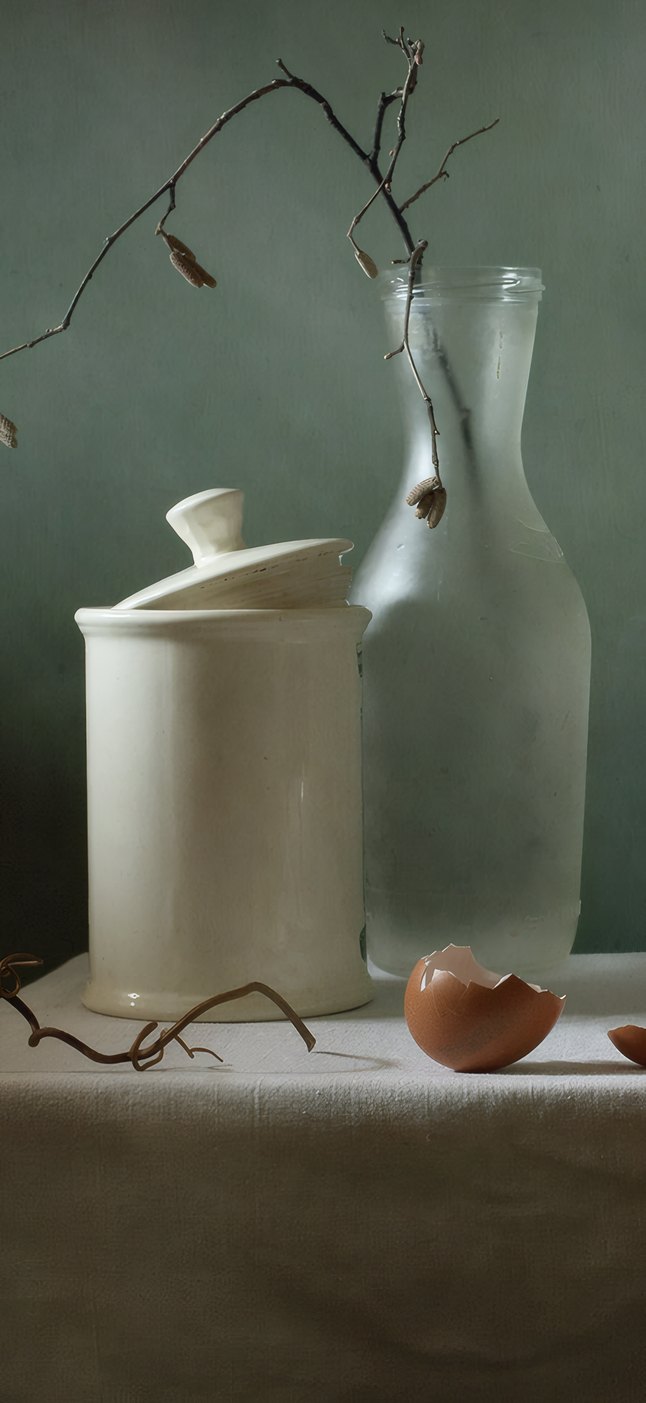 A stoneware jar and a glass carafe with a bare branch, an eggshell on linen