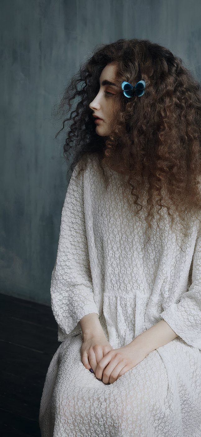 A curly-haired woman in a white knitted dress, seated, hands in her lap