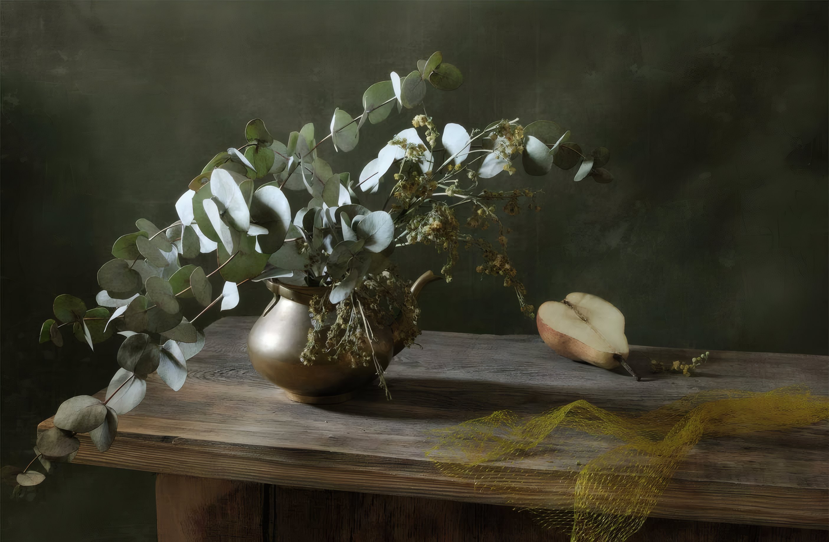 Eucalyptus branches in a brass vase beside half a pear on a weathered walnut table
