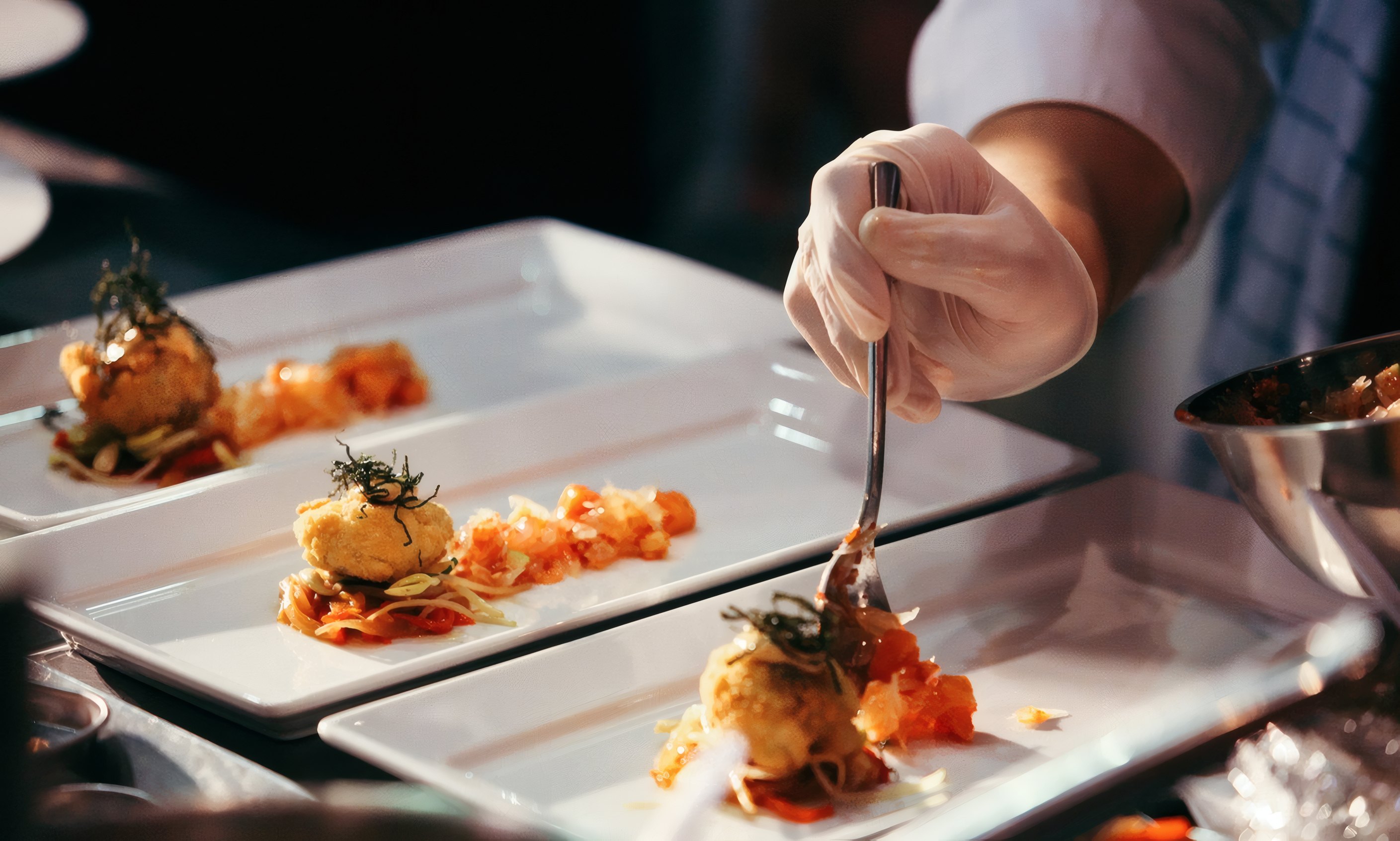 A chef plating with tweezers at the pass