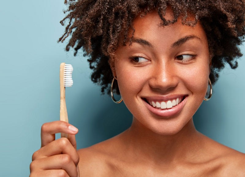 A woman smiling with a bamboo toothbrush
