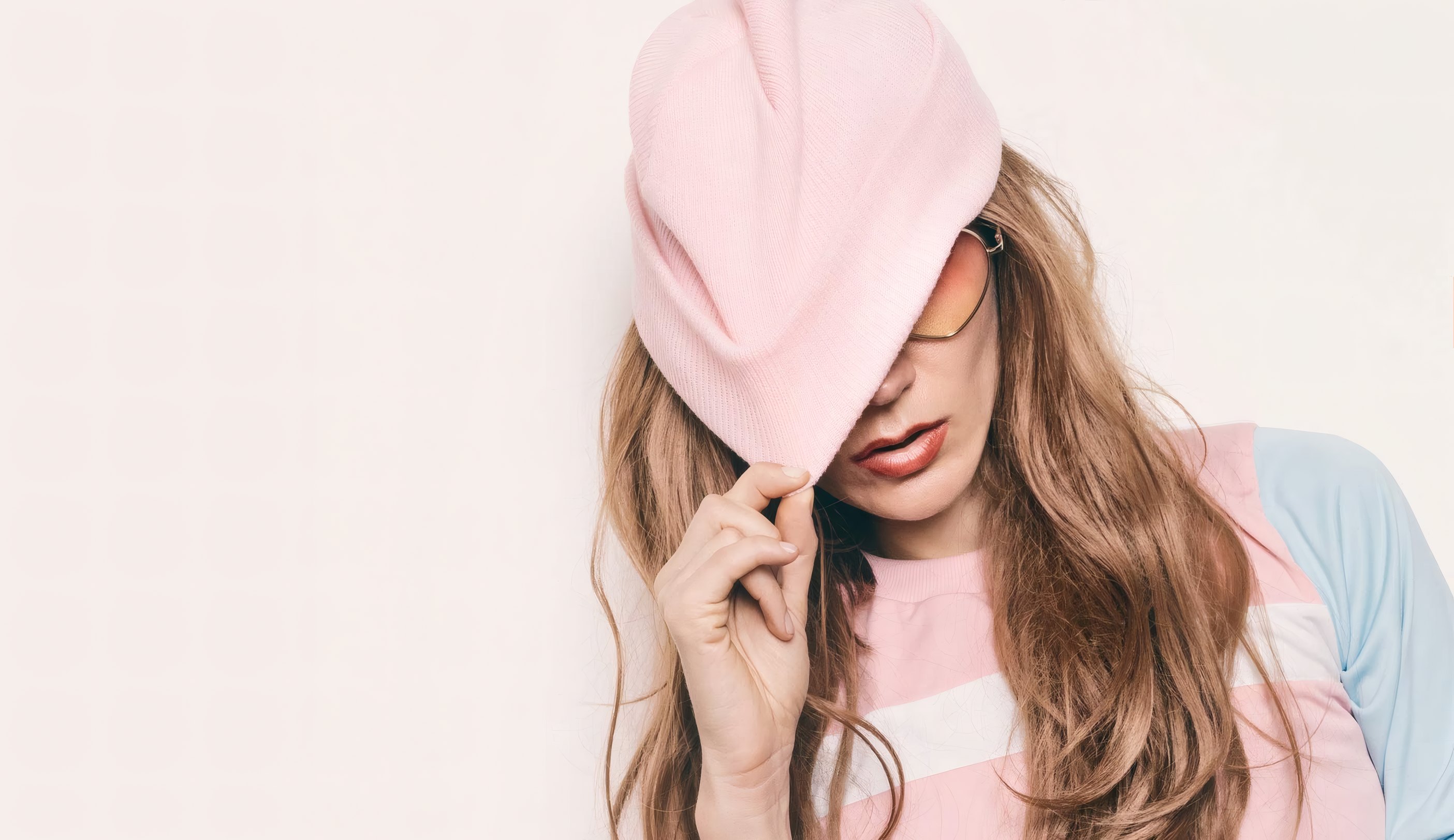 A model in a blush knit beanie against a pale pink studio wall
