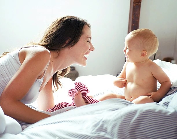 Mother laughing with her baby on a white bed