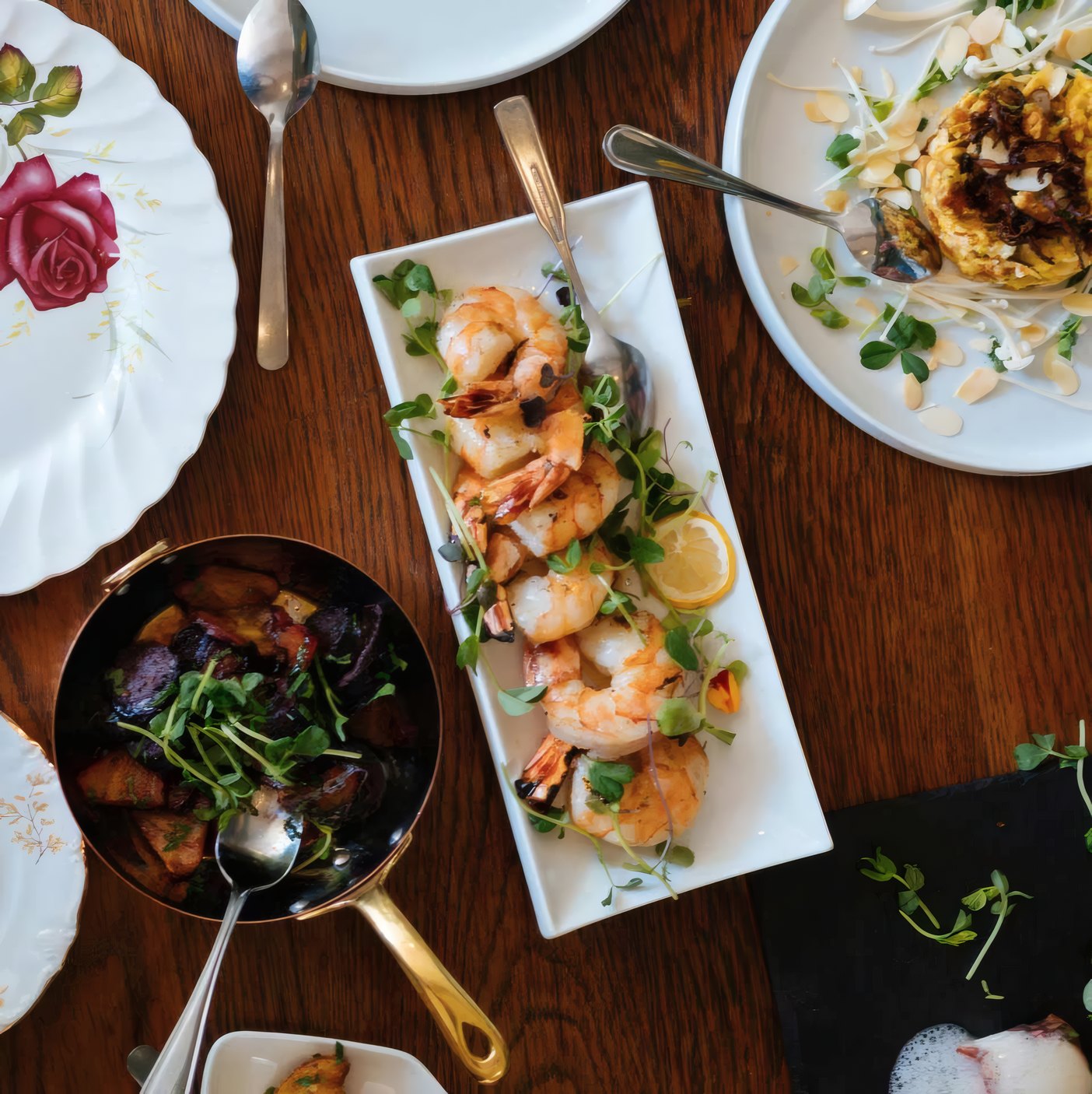 Prawns, a pan of greens and plates on a wooden table seen from above