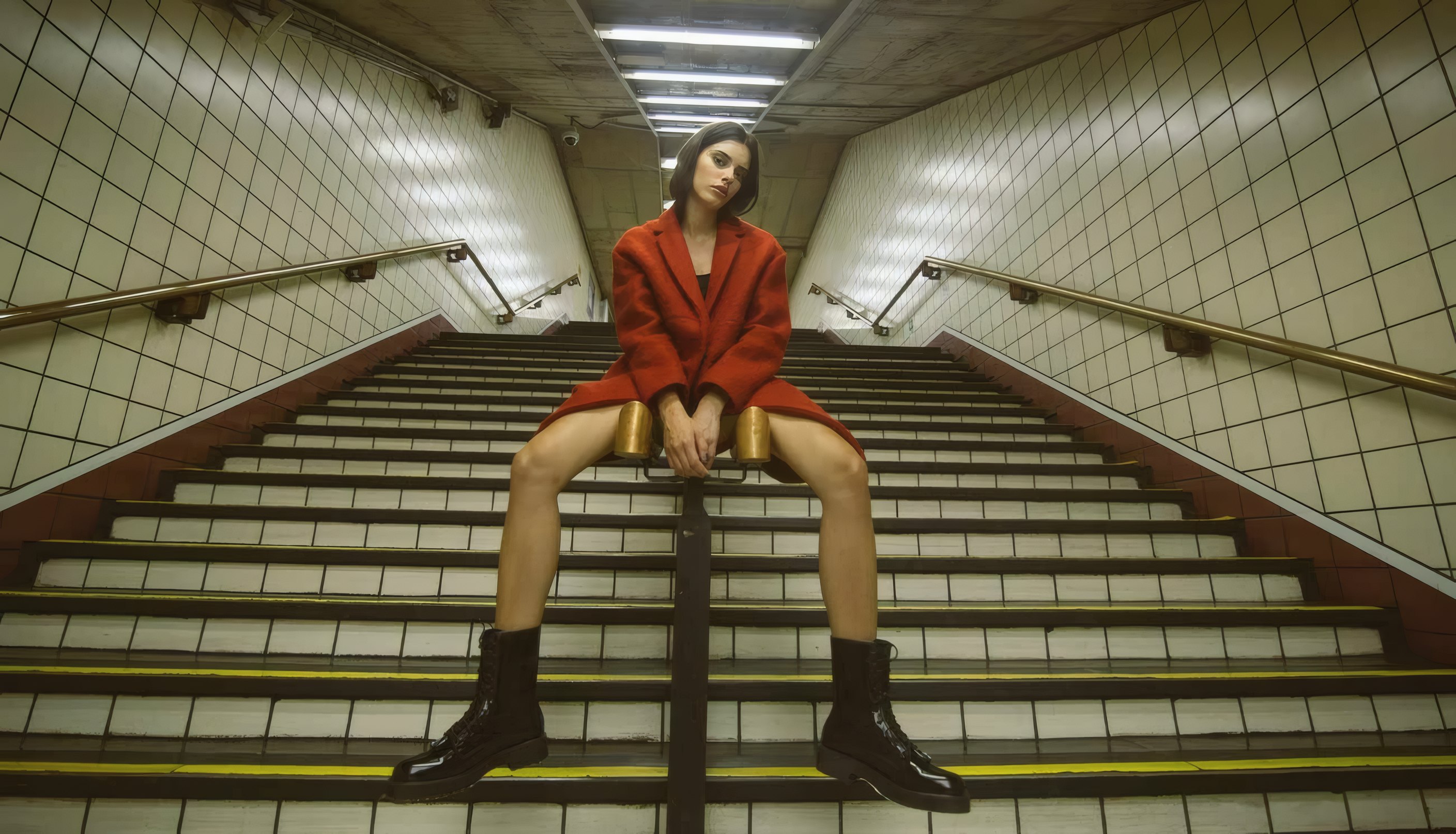 A woman in a red wool car coat sitting on the stairs of an underground station