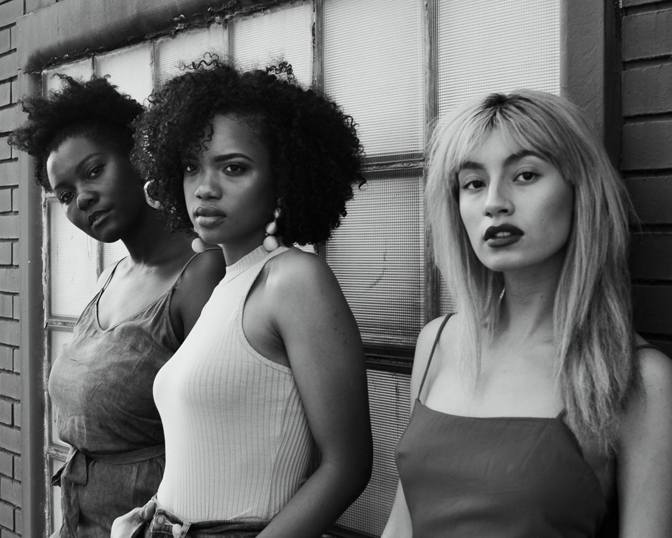 Three new faces against a brick wall, in black and white