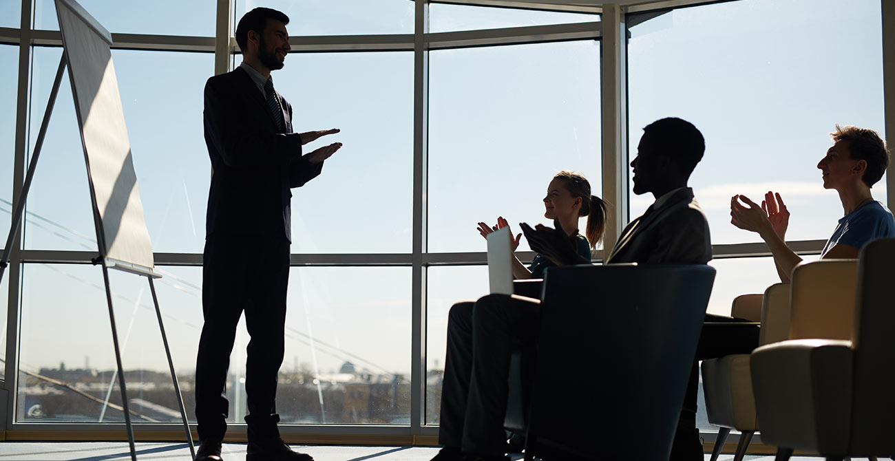 A speaker giving a talk to a small group by a tall window