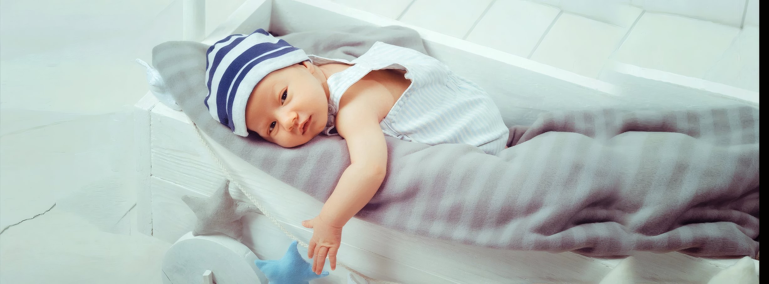 Newborn in a striped hat lying in a cot