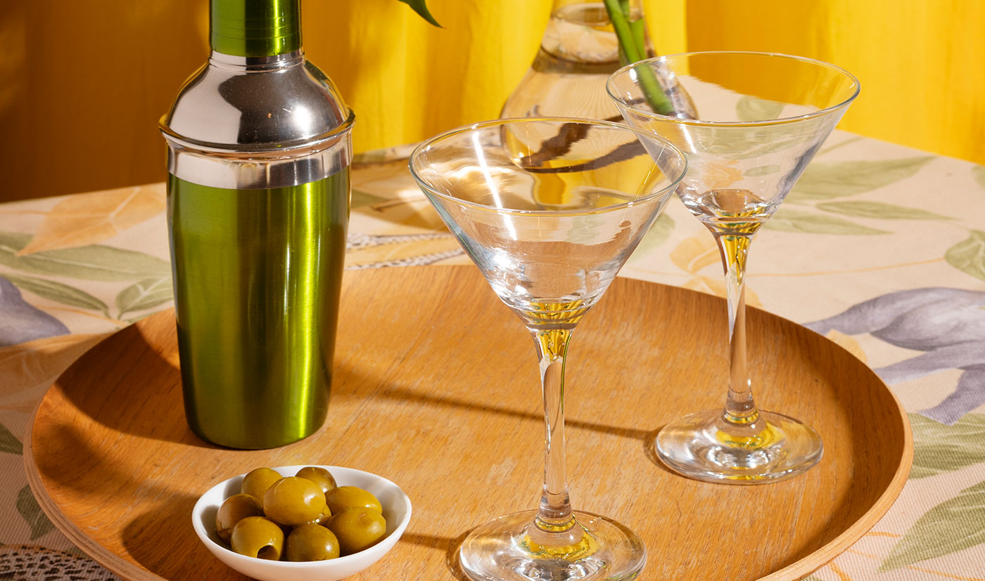 A cocktail shaker and martini glasses with olives on a tray