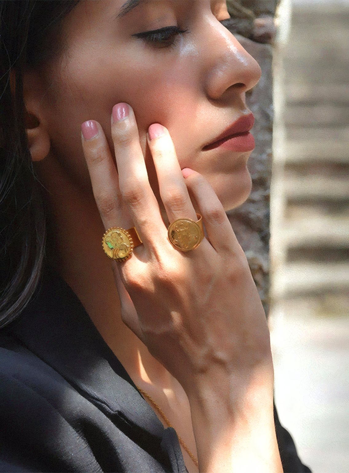 A woman resting gold rings against her cheek