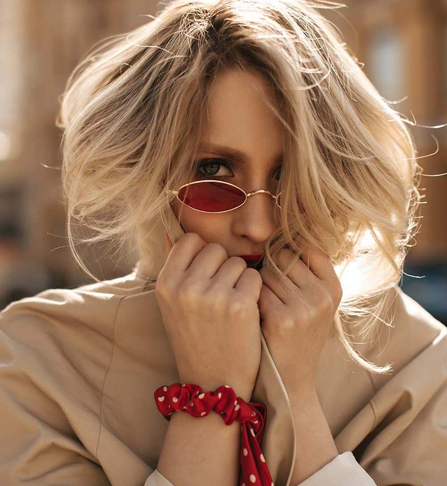 A woman in red oval sunglasses, her hands at her chin