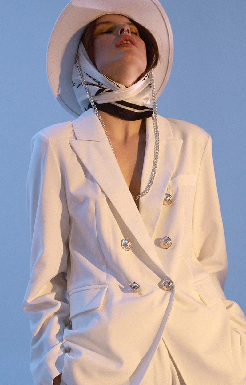 A woman in a white blazer and a wide hat against a blue sky