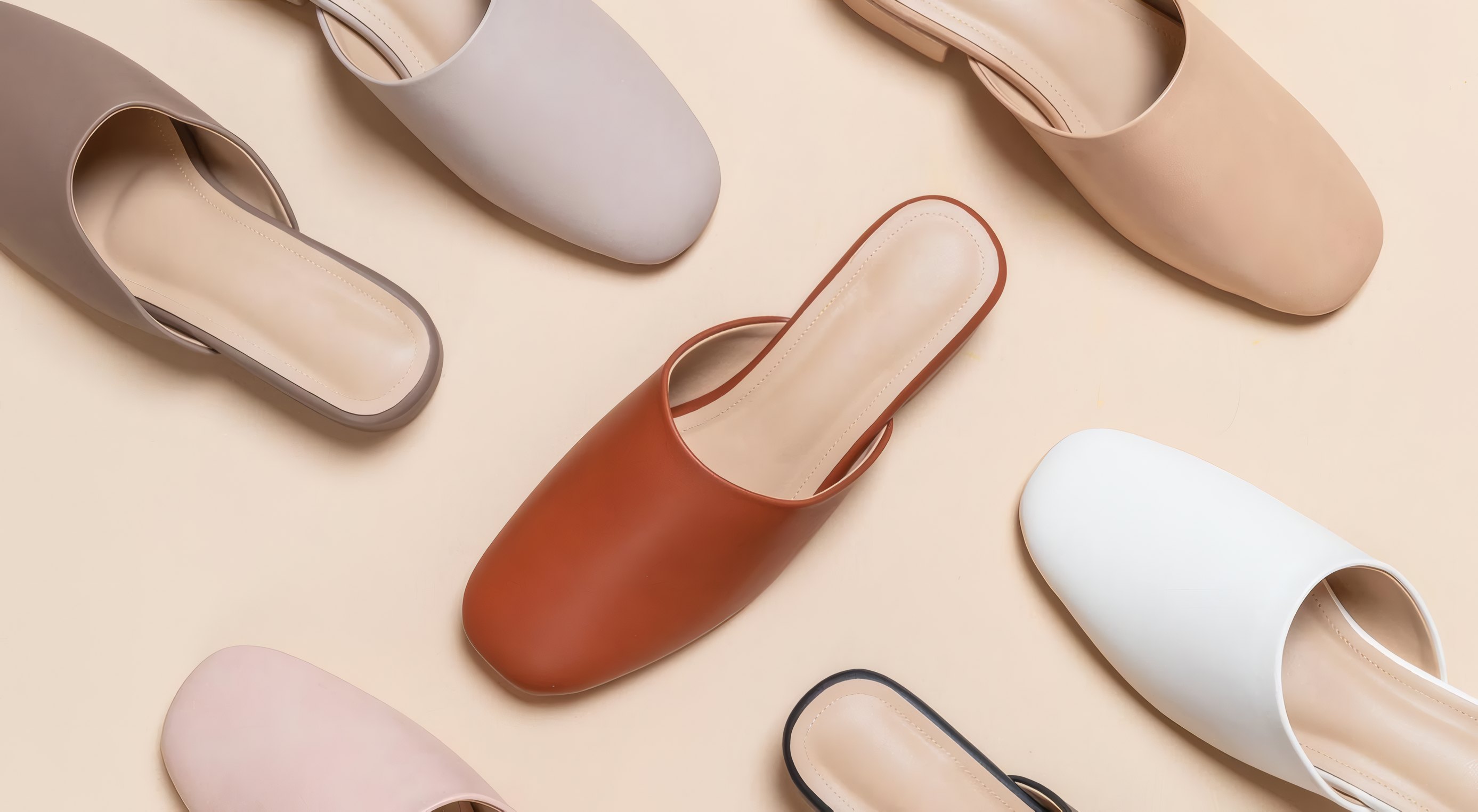 Leather mules in six colours laid out on a blush ground