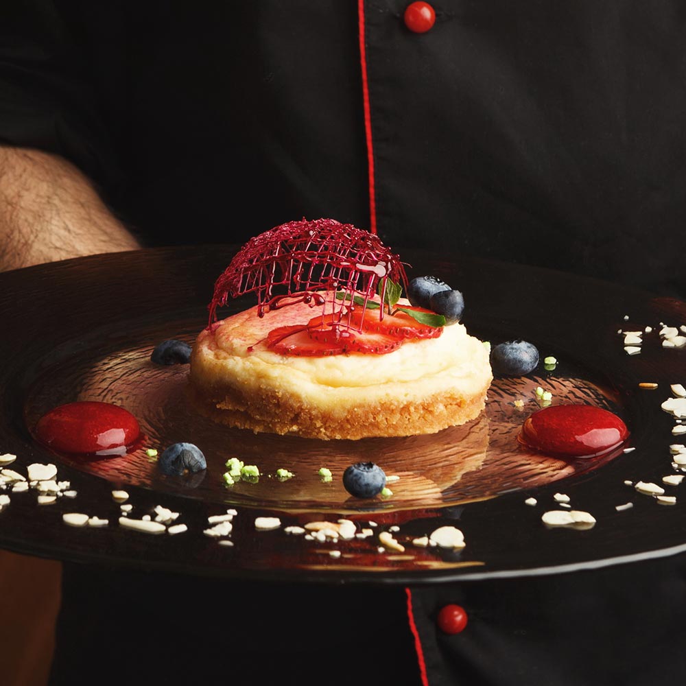 A chef presenting a plated cheesecake with berries