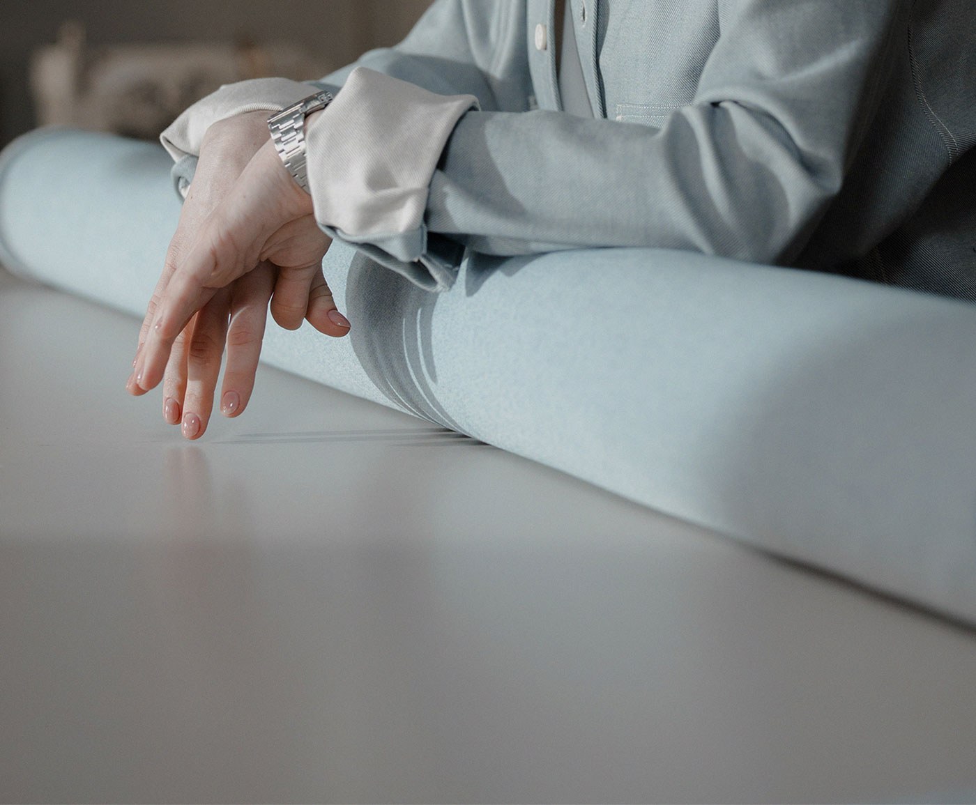 A woman in pale blue leaning on a roll of cloth