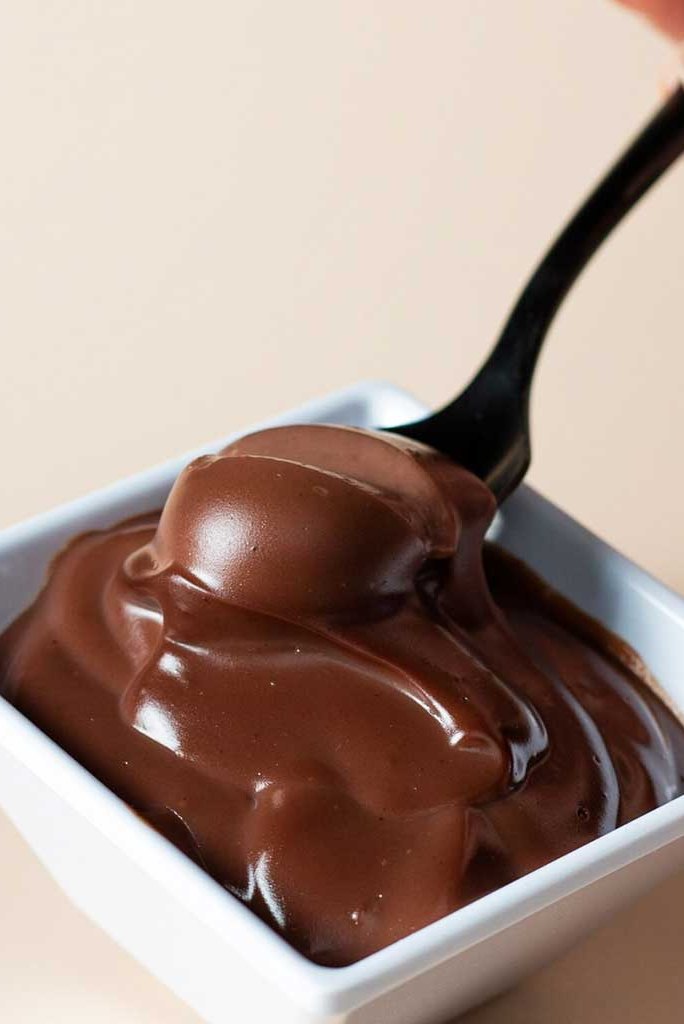 A spoon lifting melted chocolate from a white bowl