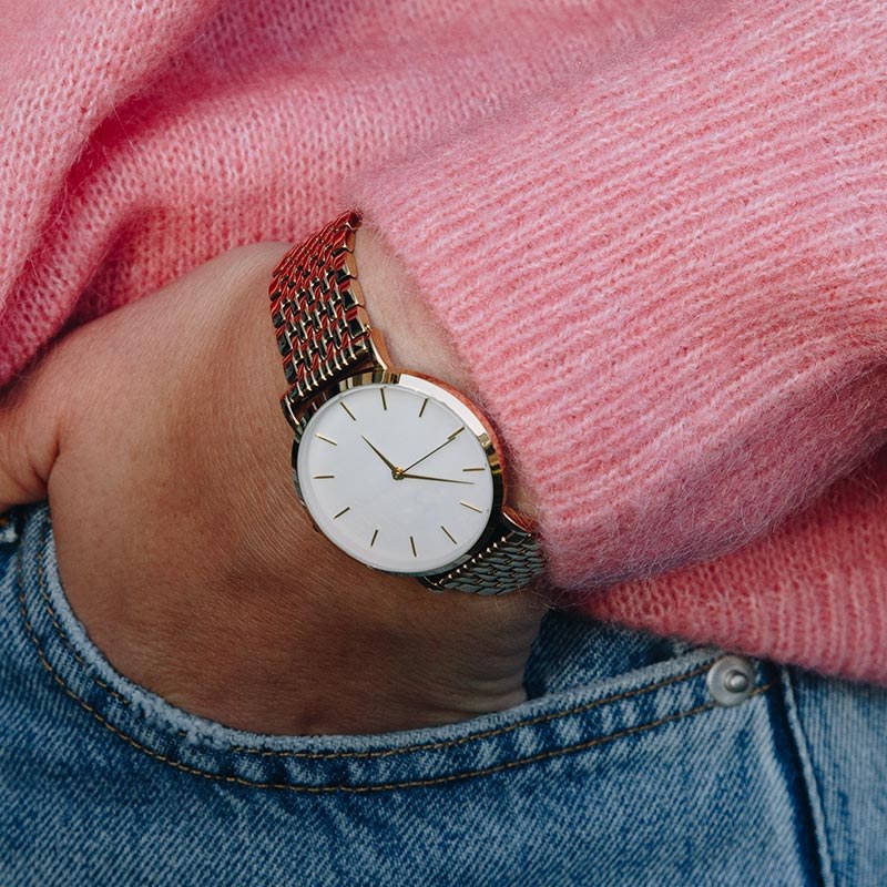A rose gold mesh watch on a wrist in a pink jumper