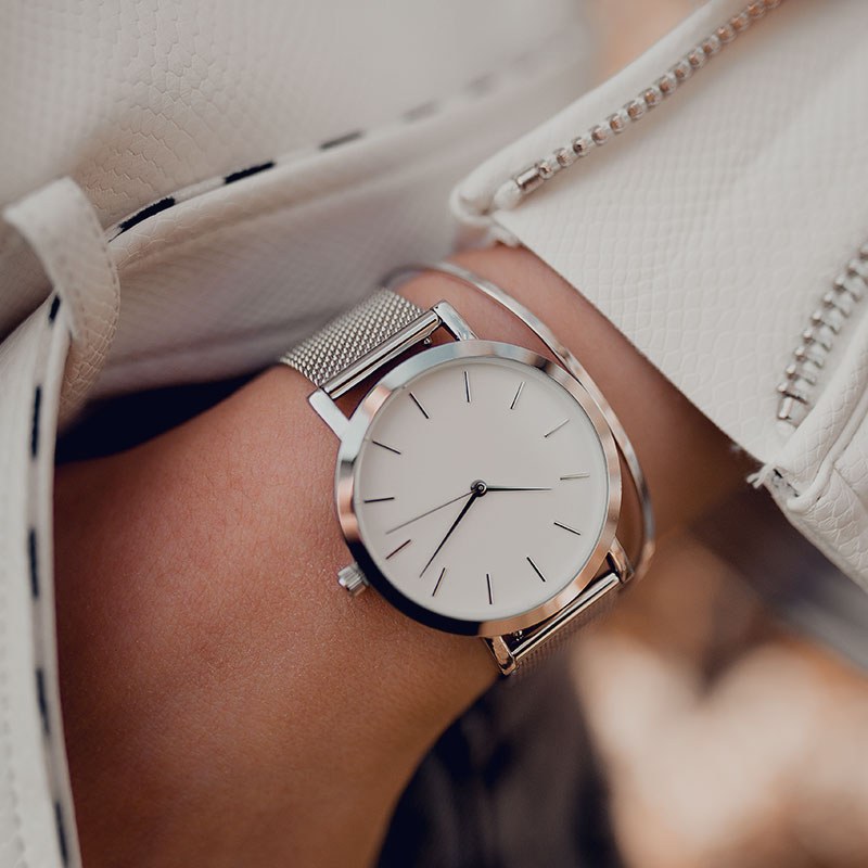 A silver watch on a wrist beside a white sleeve