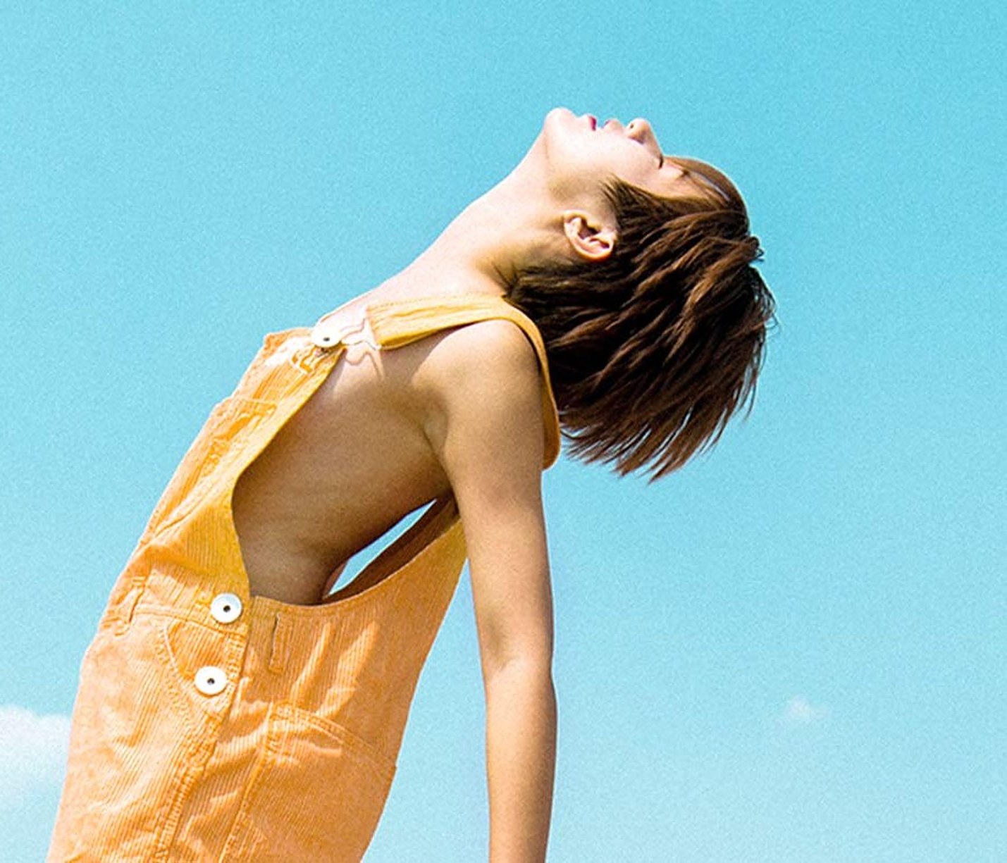 A woman in an apricot romper leaning back into the sun