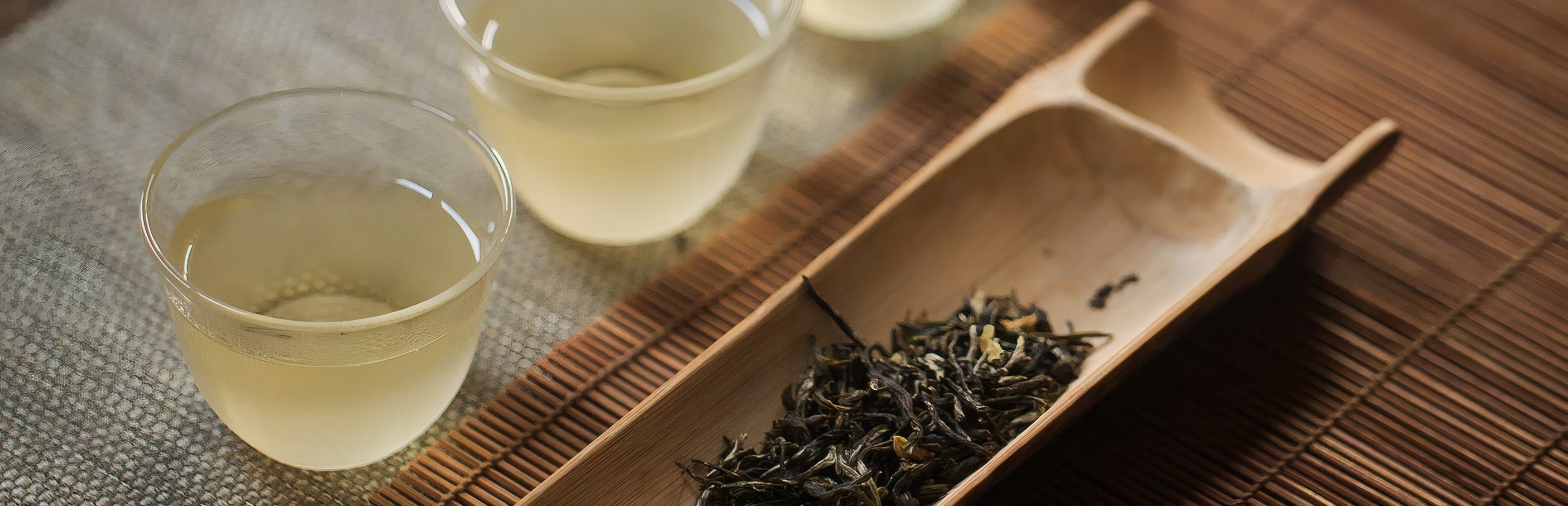 Loose leaf in a bamboo scoop beside two glasses of tea
