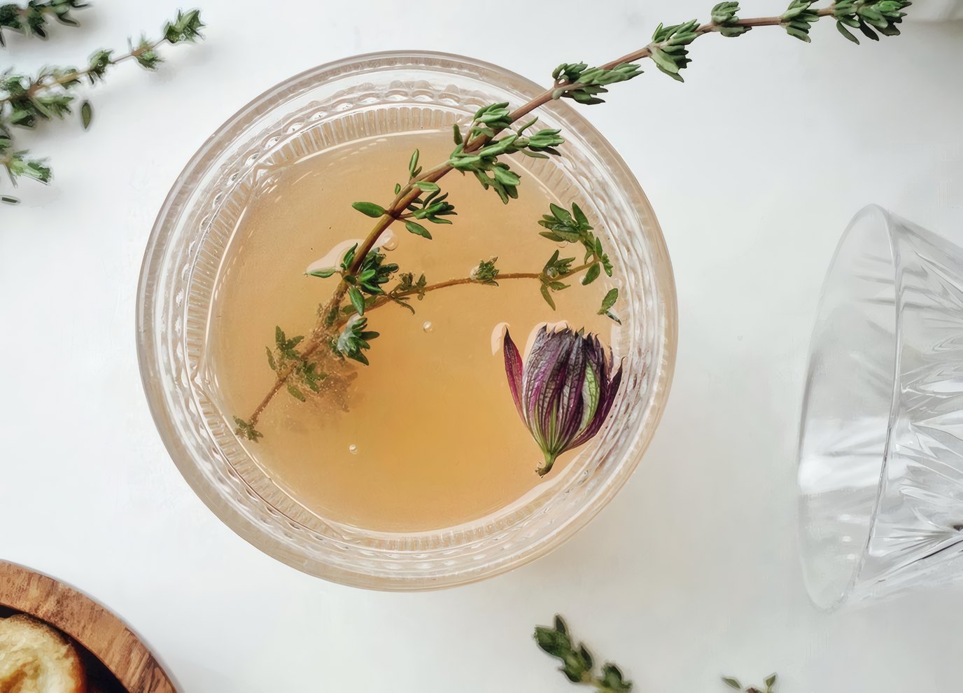 A glass bowl of tea with a sprig of thyme and a flower bud