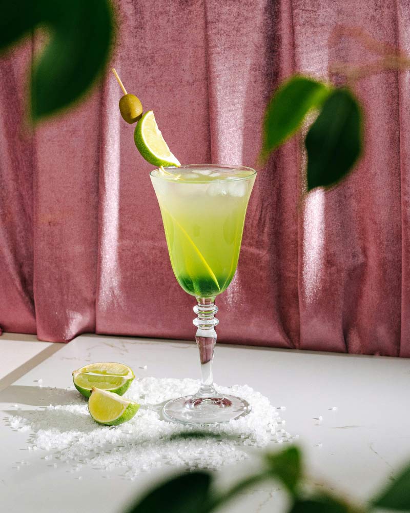 A green cocktail with lime on a pink tablecloth