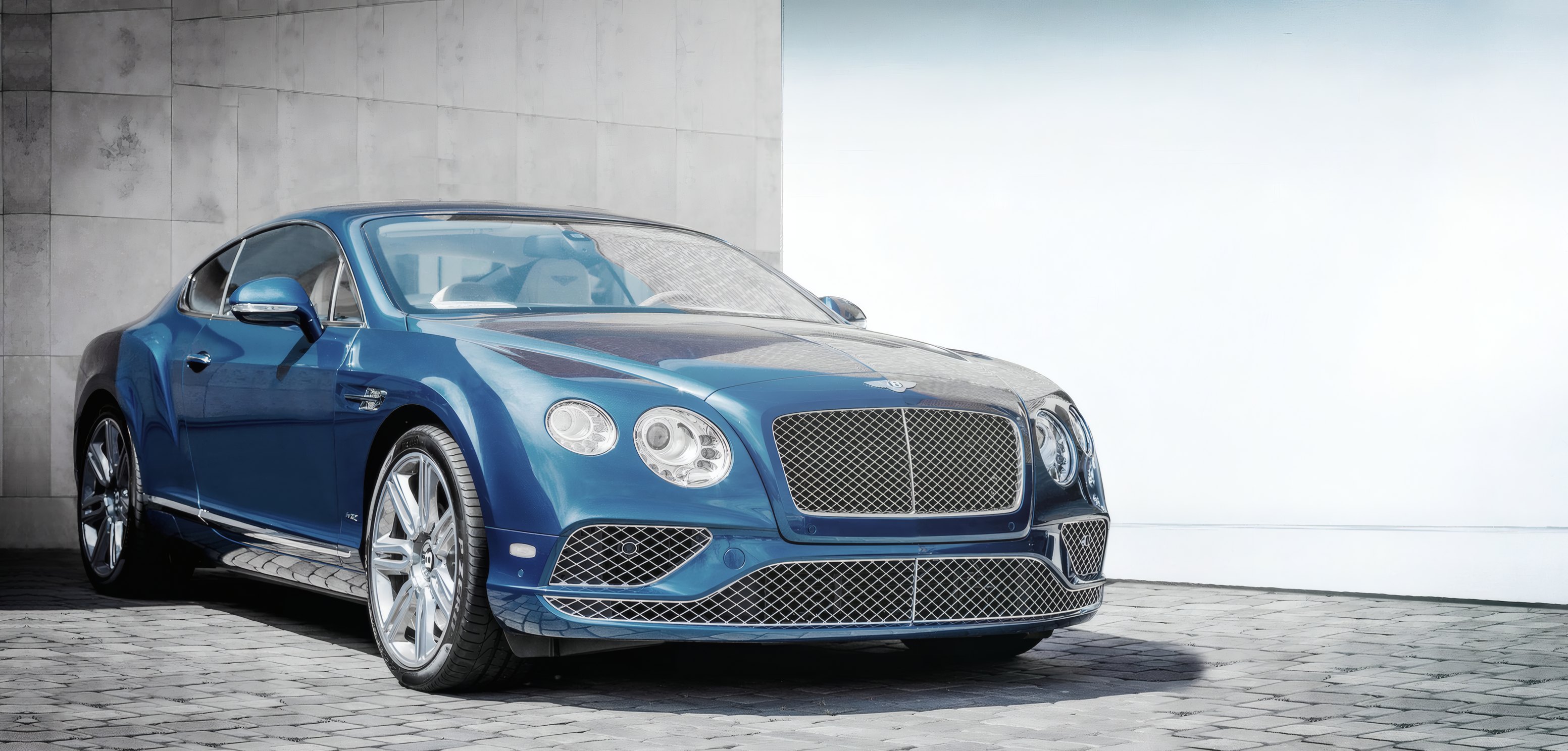 A blue grand tourer in a white studio