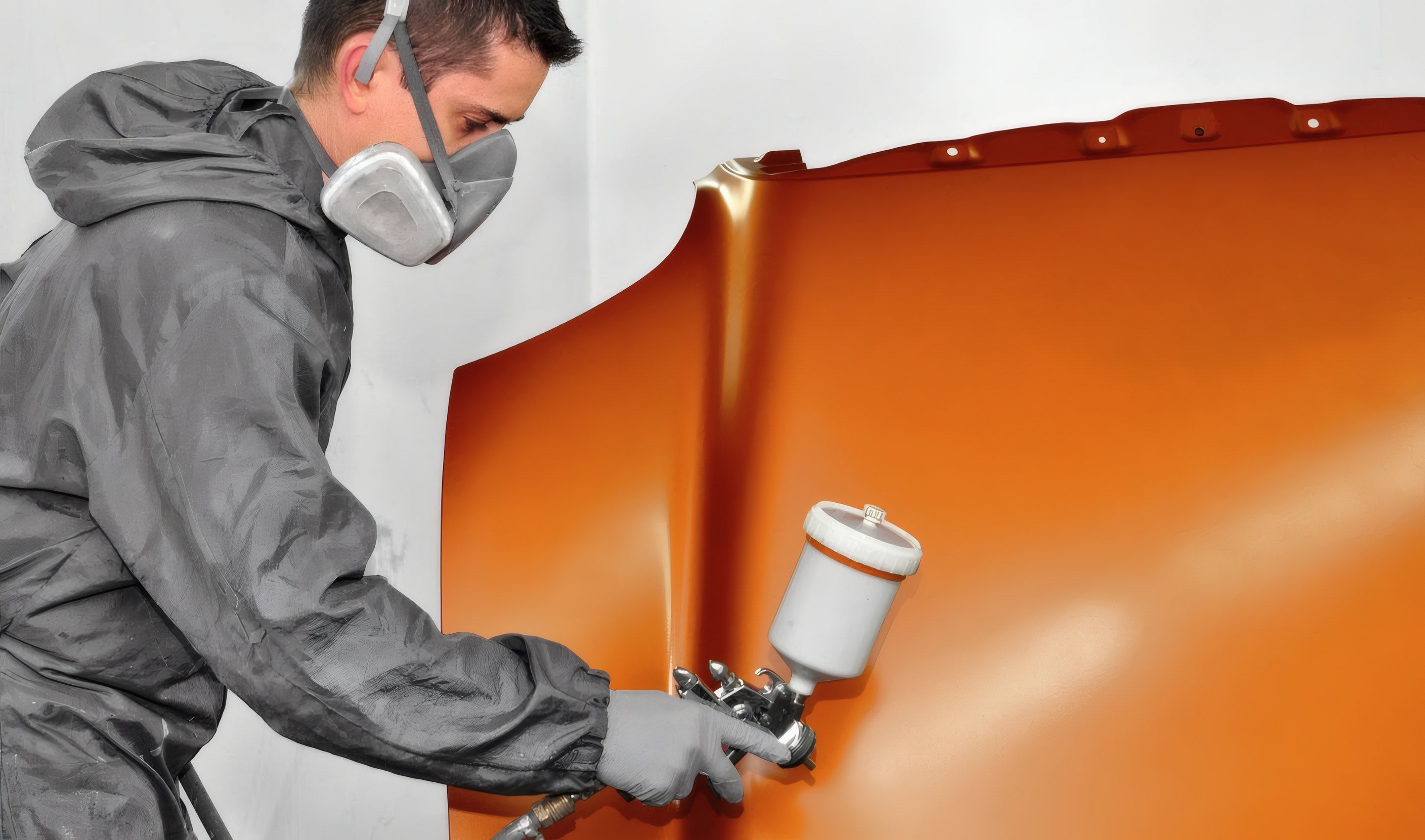 A painter in a respirator spraying an orange panel
