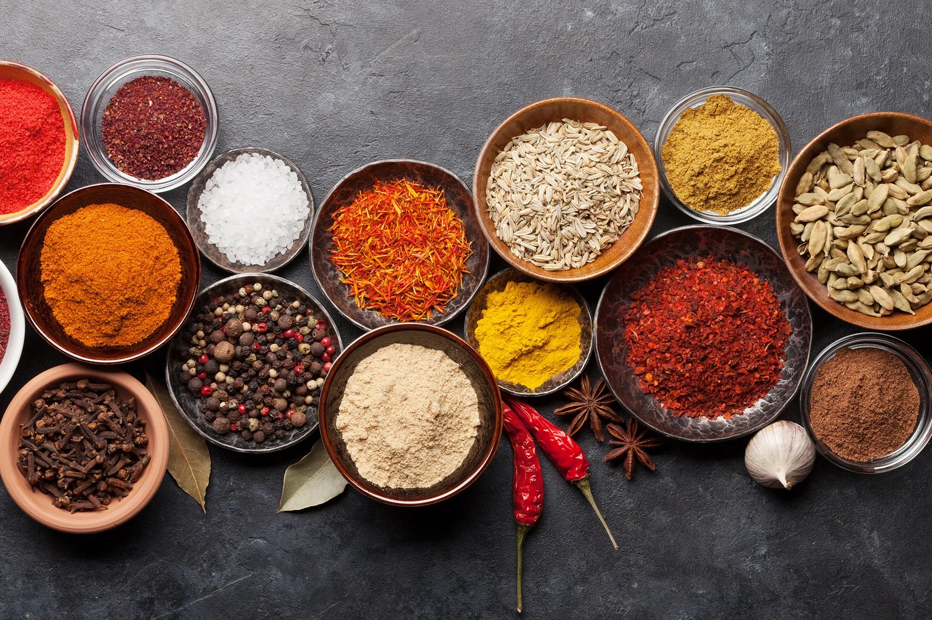 Bowls of ground spices on a dark stone counter